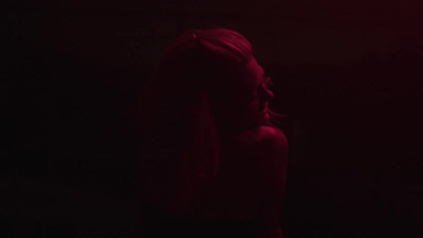 A dark silhouette of a woman with light colored hair and a bare shoulder is visible from behind as she tilts her head back and open their mouth in a smile while lit by a red light