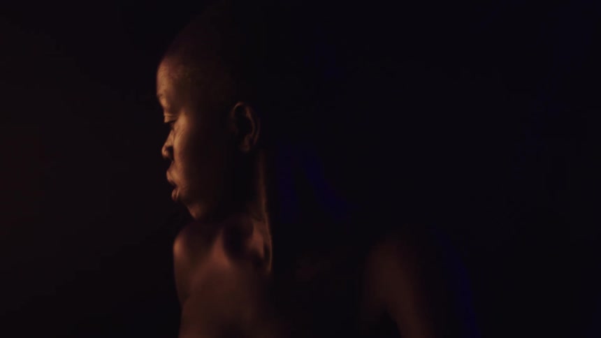 A close view of a woman with dark skin shows her turning their head in profile from left to right in a dark room