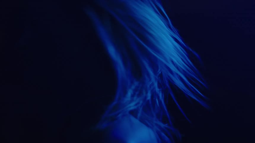 Blonde woman tosses her head while dancing in an area dimly lit by blue lighting