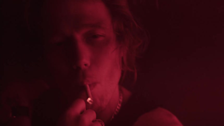 The man fills the dark room with smoke from a cigarette