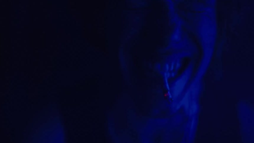 A persons face illuminated by a blue light as they exhale a cloud of smoke or vapor from a glowingtipped cigarette