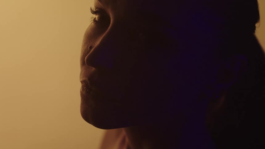 The video shows a person in profile with their face lit by a warm golden light the person appears to be speaking or emoting with their mouth slightly open