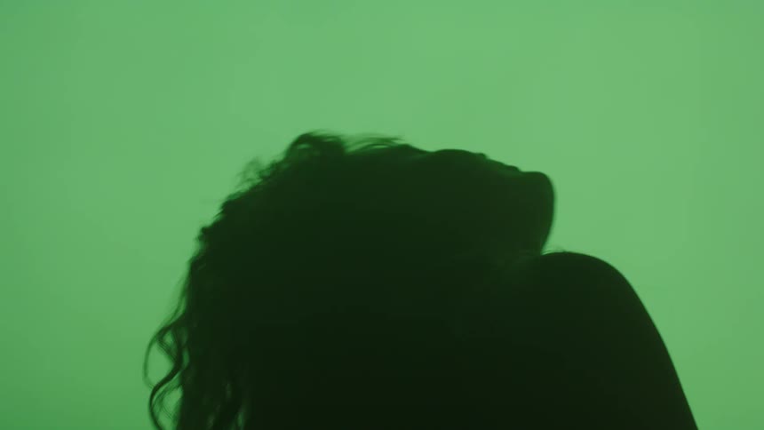A silhouetted profile of a woman with long dark hair is seen against a solid green background as her head tilts back and then forward again