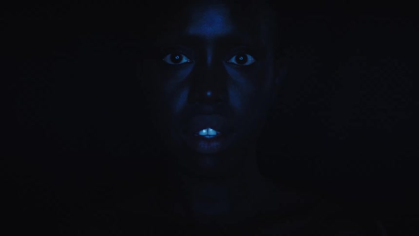 A close view of a woman with dark skin shows her face partially illuminated by a blue light