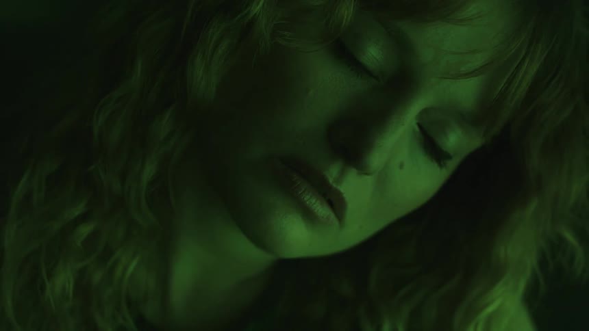 A woman with wavy hair gazes intently under moody green lighting