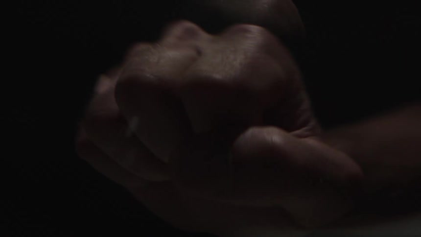 A close view shows a person clenching their hand into a fist in a dimly lit space with flashing lights