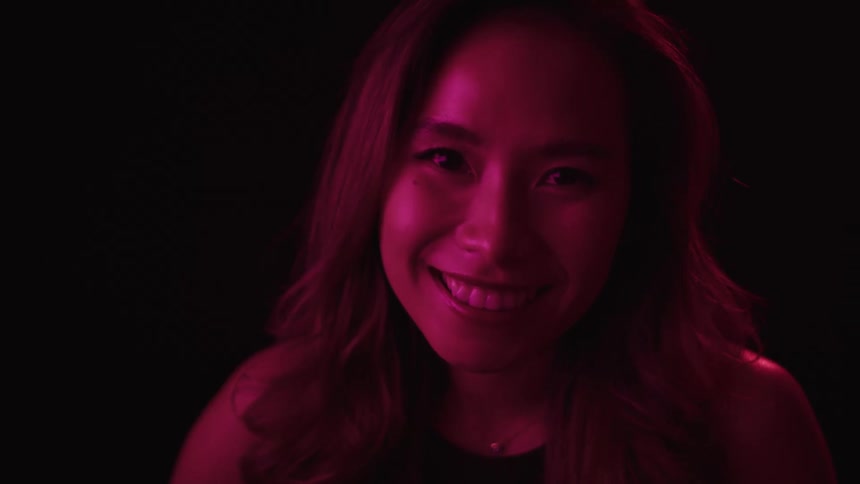 Woman smiles broadly while under maroon colored lighting