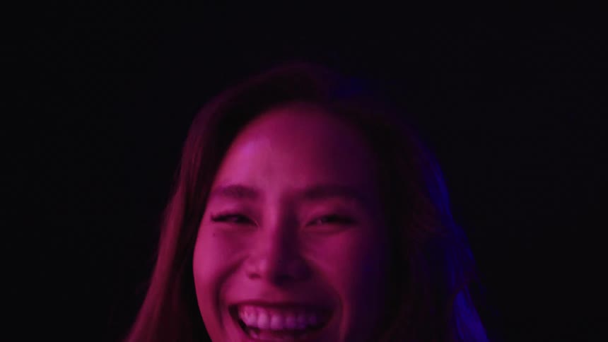 Woman smiles with closed eyes under blue light against a dark background