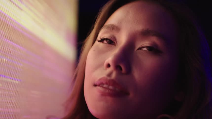 The video shows a womans face illuminated by the bright colorful light of a large led display her expression is one of awe as she looks at the pulsating lights