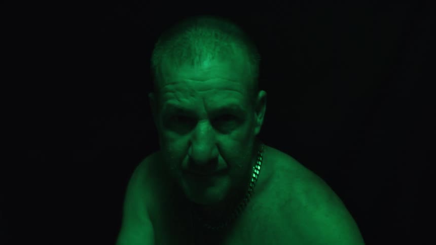 Man wearing a gold chain in a fighting stance under intense green light