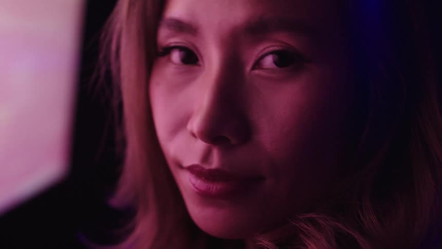 A woman looks at the camera while bright lights move behind her