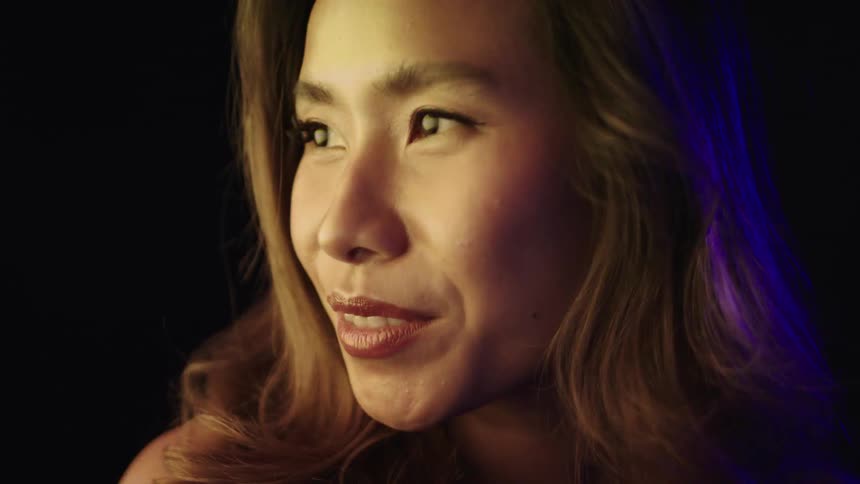 Woman smiles softly while being lit by purple and blue lights in a dark setting