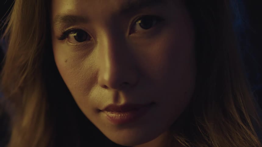 A woman is shown in a closeup portrait with warm lighting on her face and hair