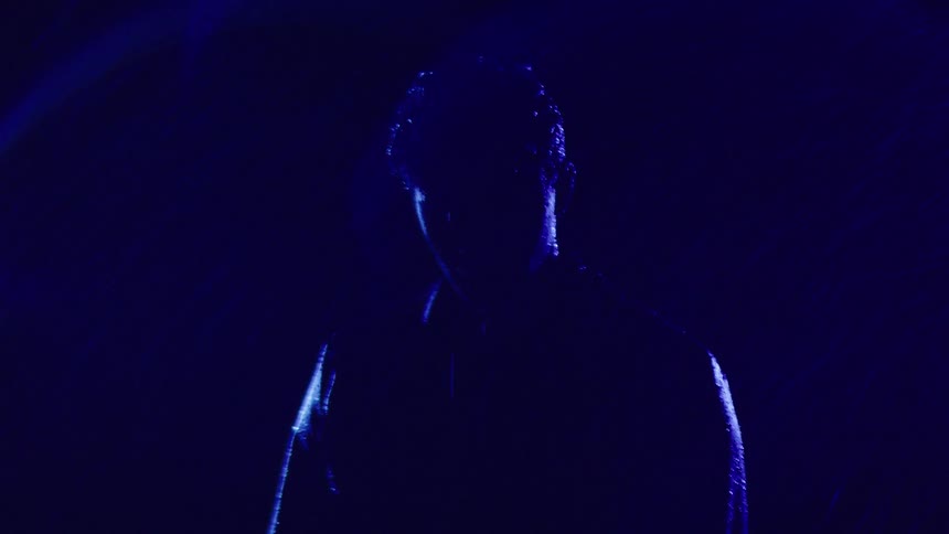 Male figure in silhouette under intense blue light in the rain