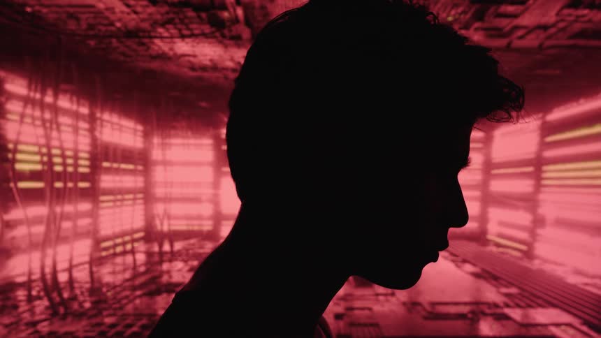 A young man walks inside a data center where the servers light up red and green casting a red glow across the room