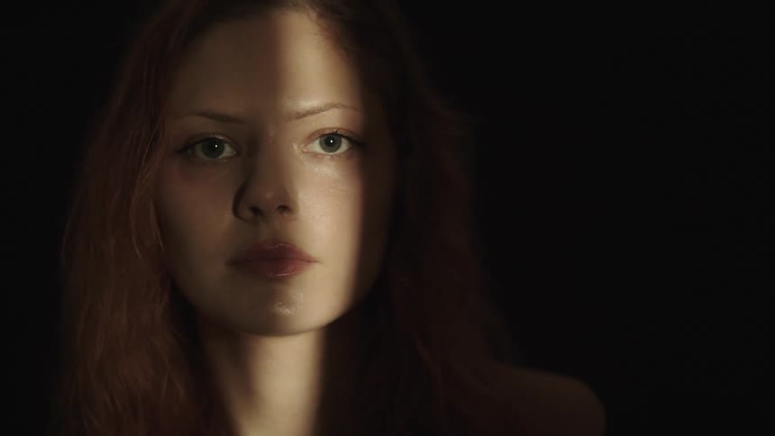 Female face lit by a slit of light amid darkness