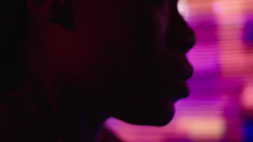 A persons face is shown in shadowed profile against a blurred backdrop of vibrant colorful lights