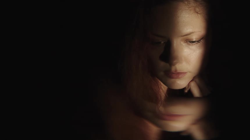 Woman with a serious expression illuminated by a beam of light in a dark environment reflected below her