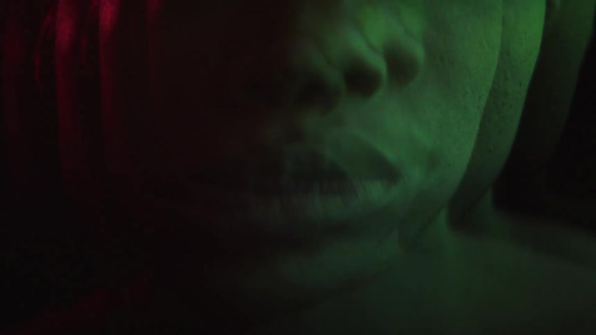 Male face lit by purple and pink light in a blurred closeup