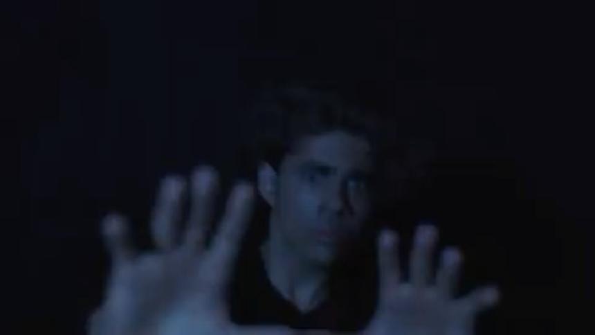 The video is dark and a mans face and hands are barely visible in a single moment suggesting he is trying to see in a lowlight environment or perhaps trying to shield his eyes from a bright flash the quickness of the shot makes it difficult to get a c