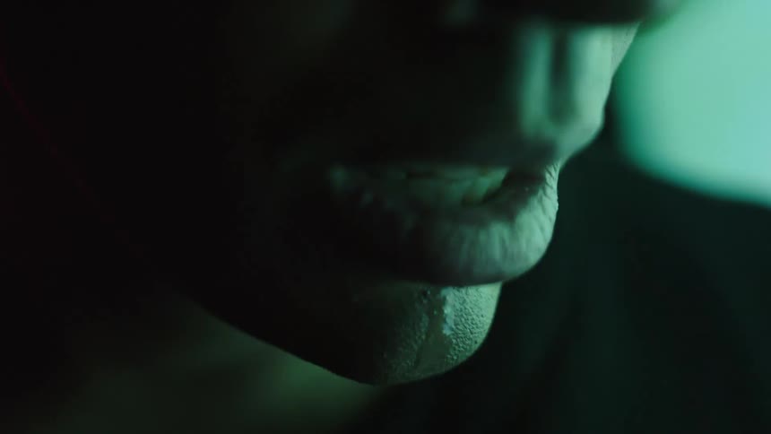 A close view shows a persons mouth and chin with a purple light illuminating the right side of the face and a red light on the left as the mouth opens to reveal the teeth and some saliva