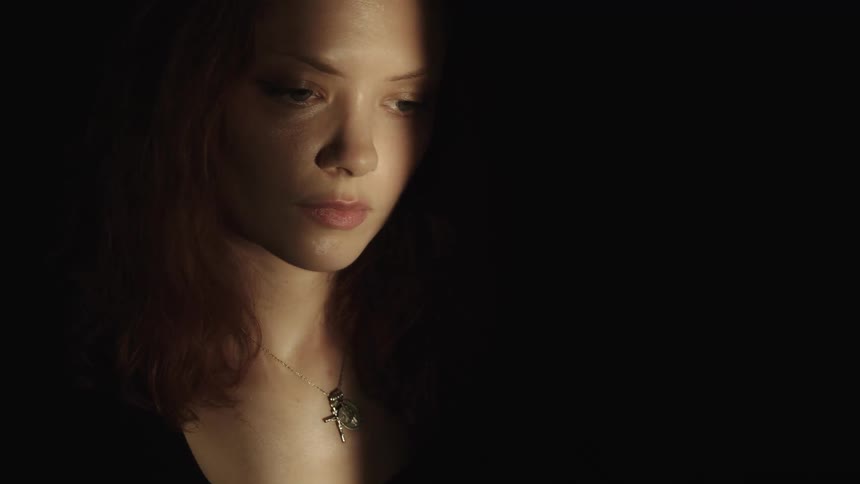 A closeup of a womans face and upper body in a lowlight setting