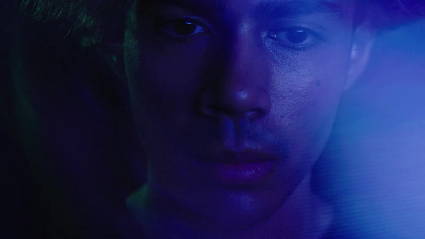 Light effects partially obscure the face of a young man illuminated by colored lighting while standing in the dark