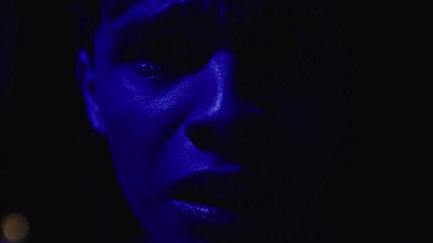 Closeup of a persons face being revealed and then obscured by a pulsating blue light in a dark setting