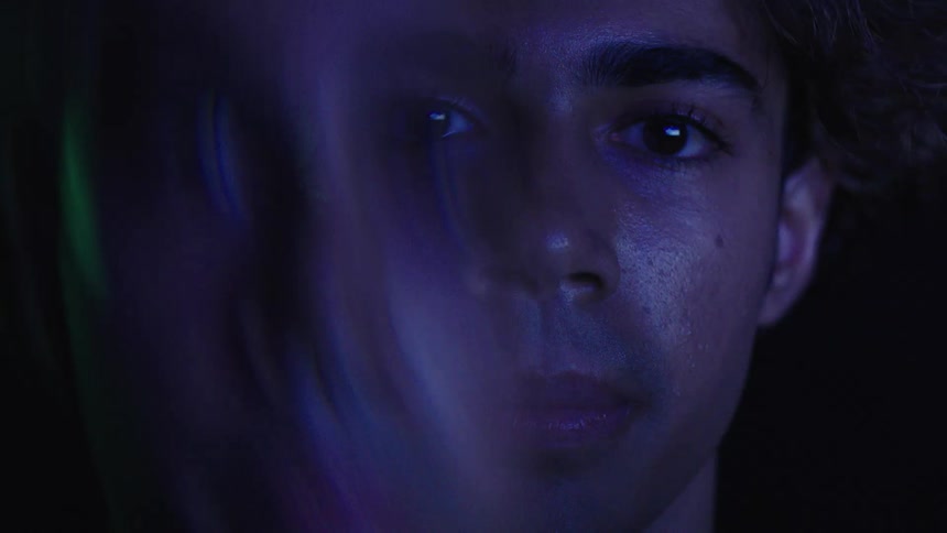 Face of a young man illuminated by blue and green light in a dark setting