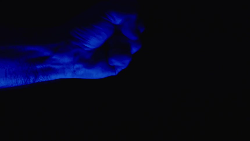 A person opens and closes their hand which is illuminated with blue light