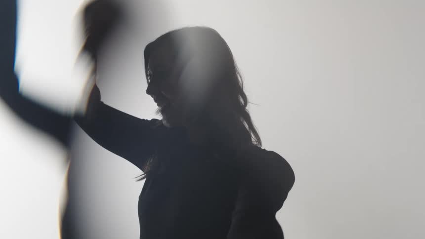 A silhouette of a woman is shown against a bright background with her profile visible while she is dancing