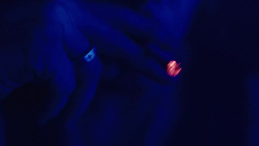 A man in a dark room only a blue light partially falling on him smokes a cigarette