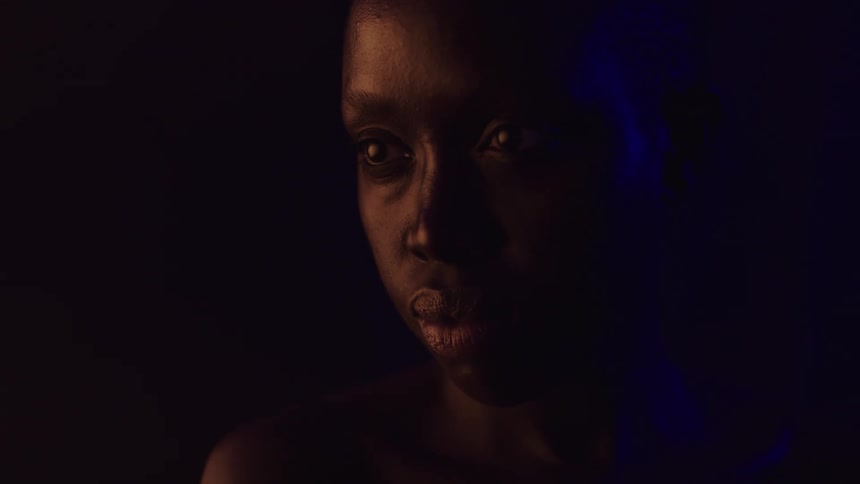 A person in the dark looking serious then their eyes dart to the side