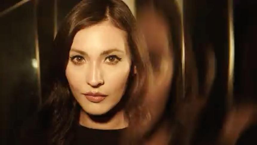 Woman in focus with a blurred reflection beside her in a goldenlit setting  under flashing lights
