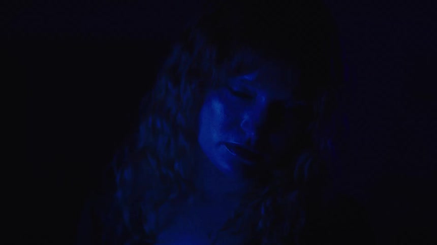 Woman lit by intense blue light stares at the camera in a dark setting