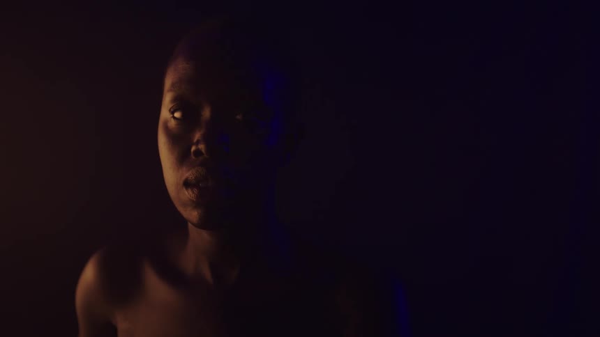 A young black woman is looking to the camera in a dark room