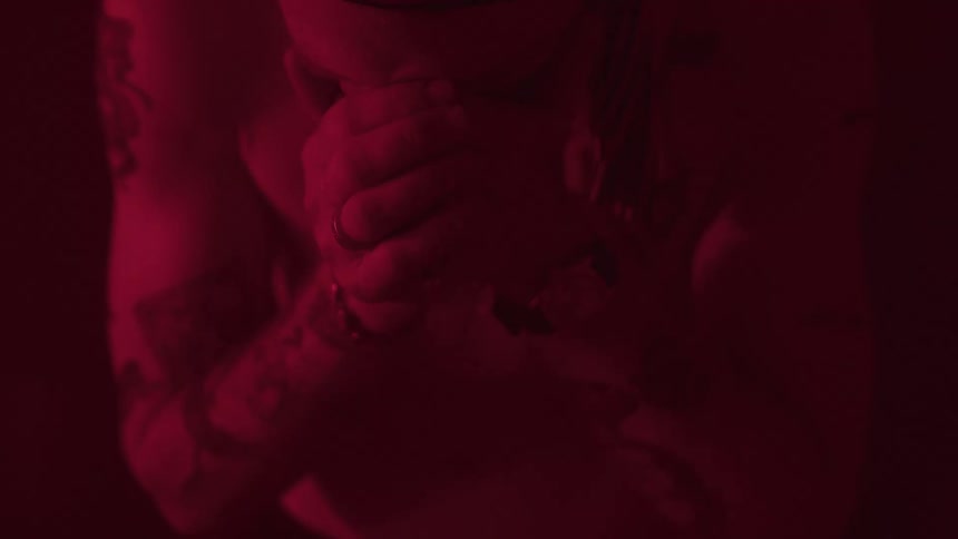 Tattooed man covering his face with his hands under red light