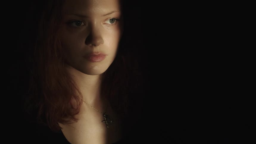 Close up portrait of a young woman standing behind a door opening in a dark room