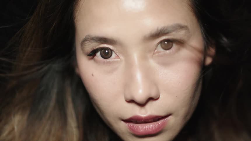A closeup of a womans face with a somber expression illuminated by a moody light combination