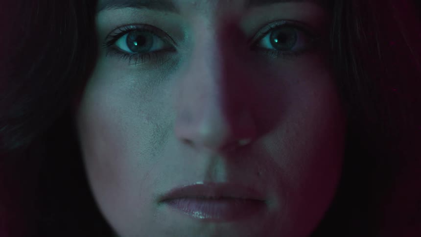 A closeup of a womans face is lit with blue and red light