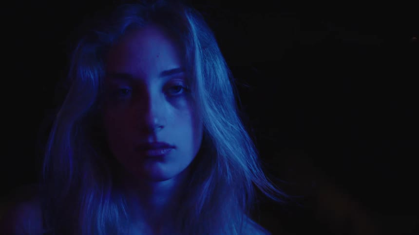 A blonde woman is looking directly at the camera with a serious expression