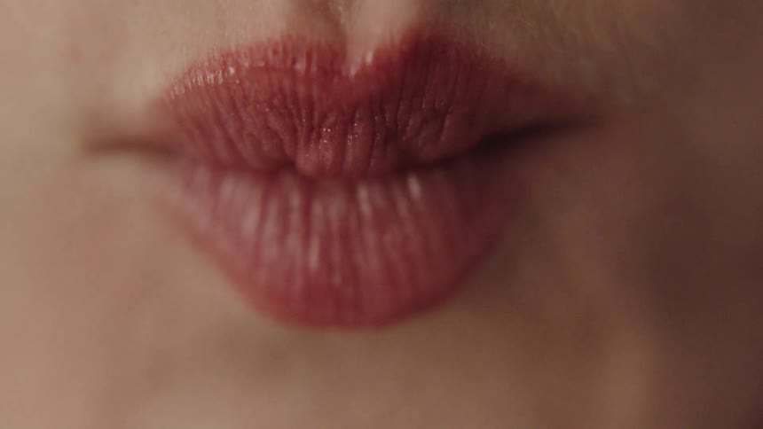 A womans lips are shown pursing and puckering she has smooth skin and dark red lipstick
