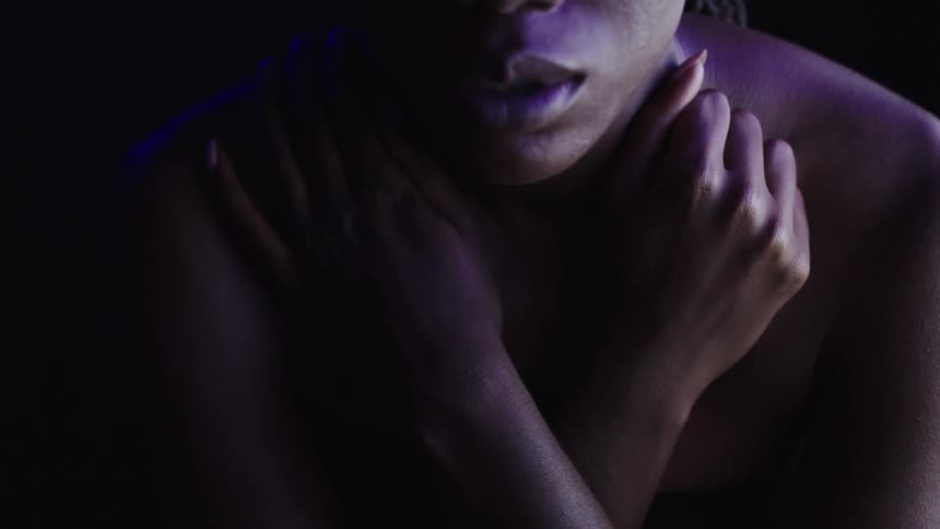 Blurry effect temporarily obscures a woman crossing her arms near her neck in an area lit by colored lighting