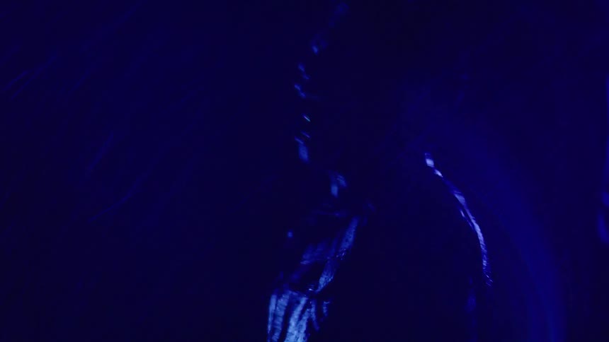 The video shows a dark abstract scene with streaks of blue light moving on a black background the lights seem to be forming a vaguely human shape