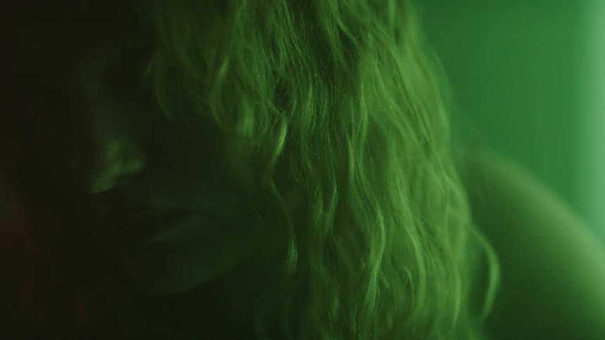 Blonde woman turns her head to face forward in a room lit by a pale green light