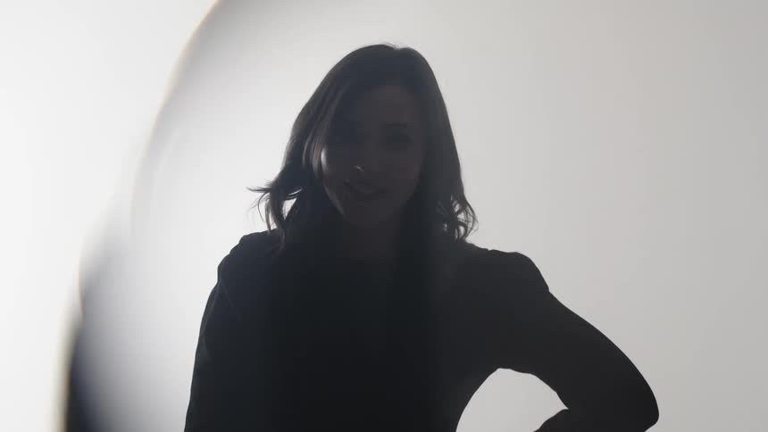 A smiling woman gestures and puts her hand on her waist behind lens effects