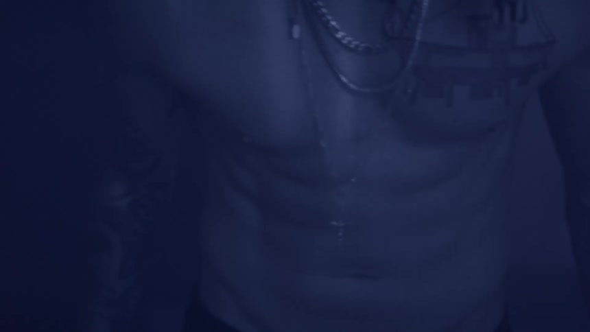 Chest of a muscular man wearing necklaces in the dark