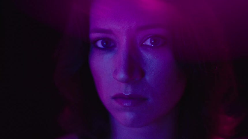 A womans face is illuminated with purple light as distortion warps her appearance