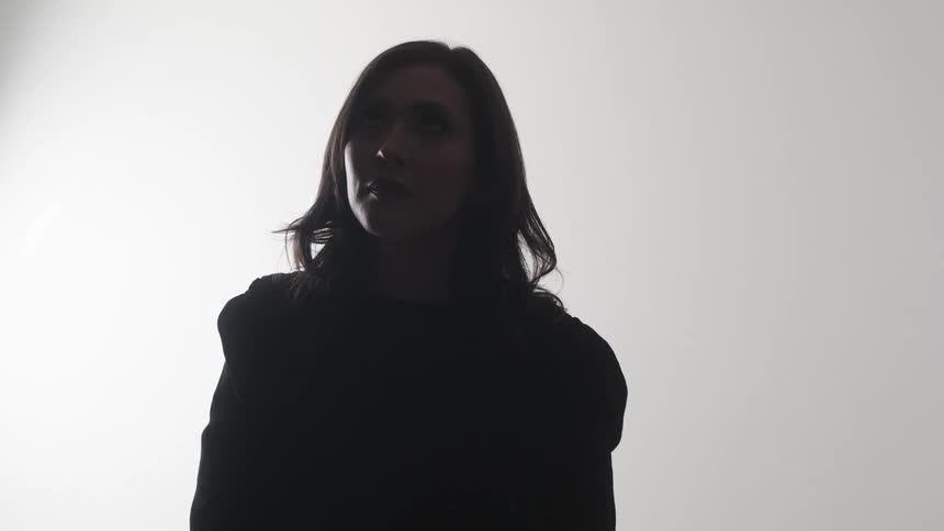 A woman with dark hair stands in silhouette against a bright white background with a lens distorting her shape