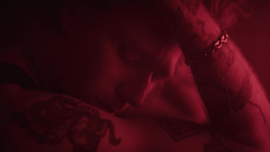 A moody and closeup shot of a muscular tattooed individuals torso and arm highlighted by a stark red light